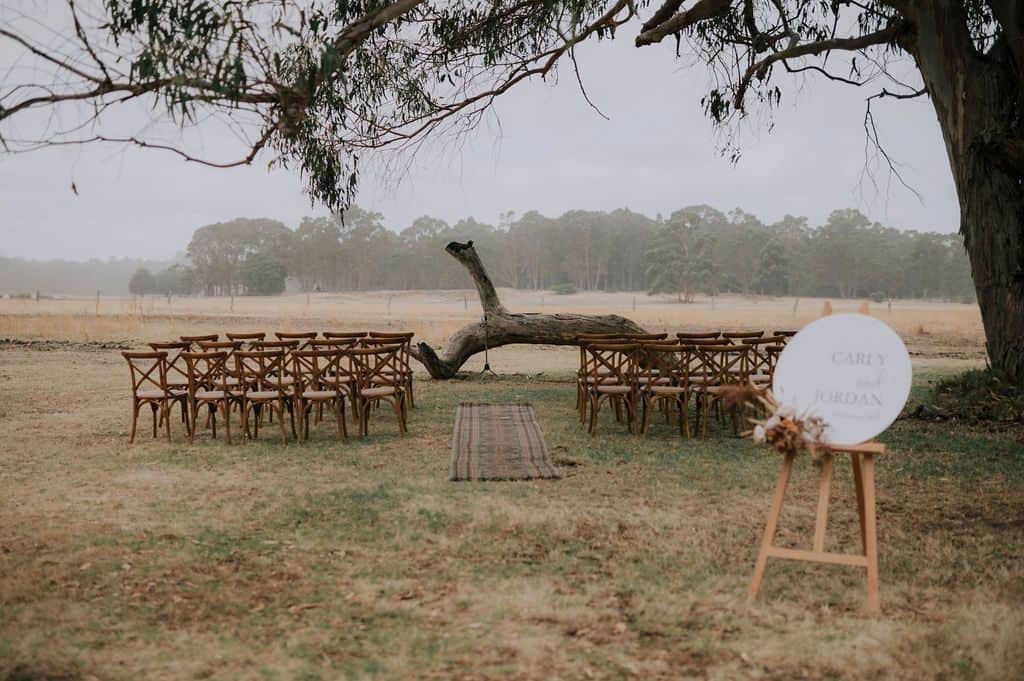 Picture of a beautifully set up wedding ceremony at the Margaret River Retreat. Delicate branches hang overhead, creating a natural canopy, while the vast paddocks and the quintessential Australian bush provide a serene backdrop. This image encapsulates the rustic charm and breathtaking beauty of a Margaret River wedding venue