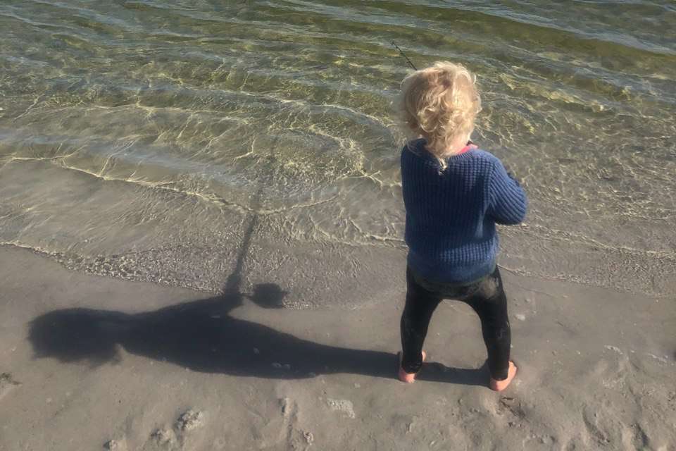 A young child stands at the edge of the clear waters of Margaret River, gazing into the water, possibly looking at fish, symbolizing the beginning of an interest in Margaret River fishing.