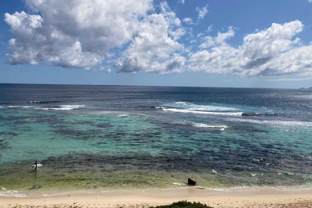 A tranquil view of Yallingup Beach showcasing the clear turquoise waters with gentle waves, a pristine sandy shore, and a vibrant blue sky dotted with fluffy clouds.