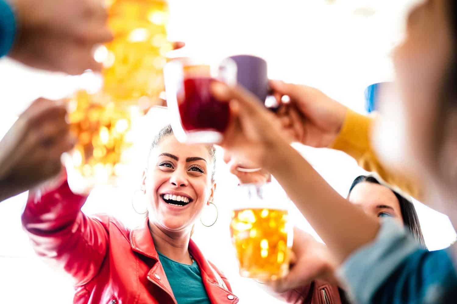 A group of friends standing as a group and enjoying their beers at a brewery in Margaret River. They raise their glasses for a cheers, with happy expressions on their faces and the brewery's ambient lighting creating a warm atmosphere.