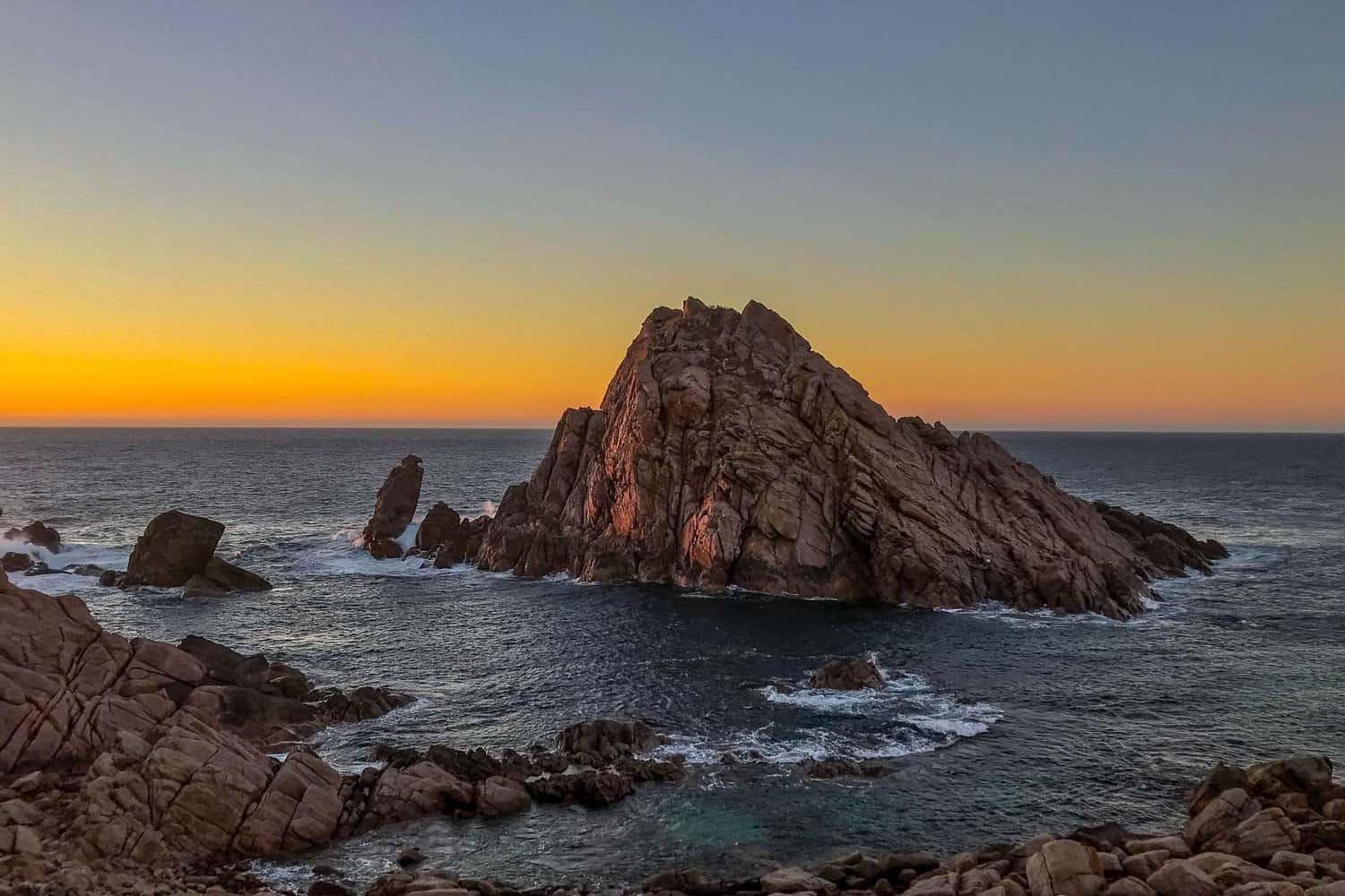 Sunset hues casting a warm glow over the ancient rock formations along the Margaret River coastline, a sight of natural wonder.