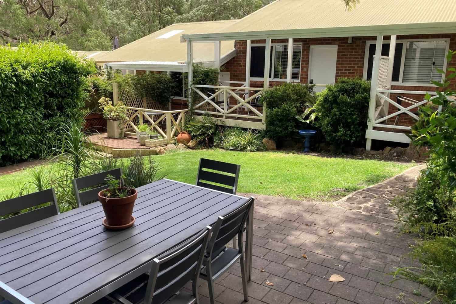 Courtyard at Edge of the Forest Motel featuring a shaded seating area with chairs around a table, with motel rooms visible in the background.