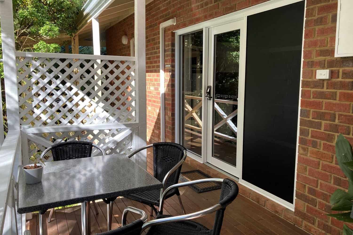 Shaded balcony area at Edge of the Forest Motel with rooms in the background and chairs arranged around a table.