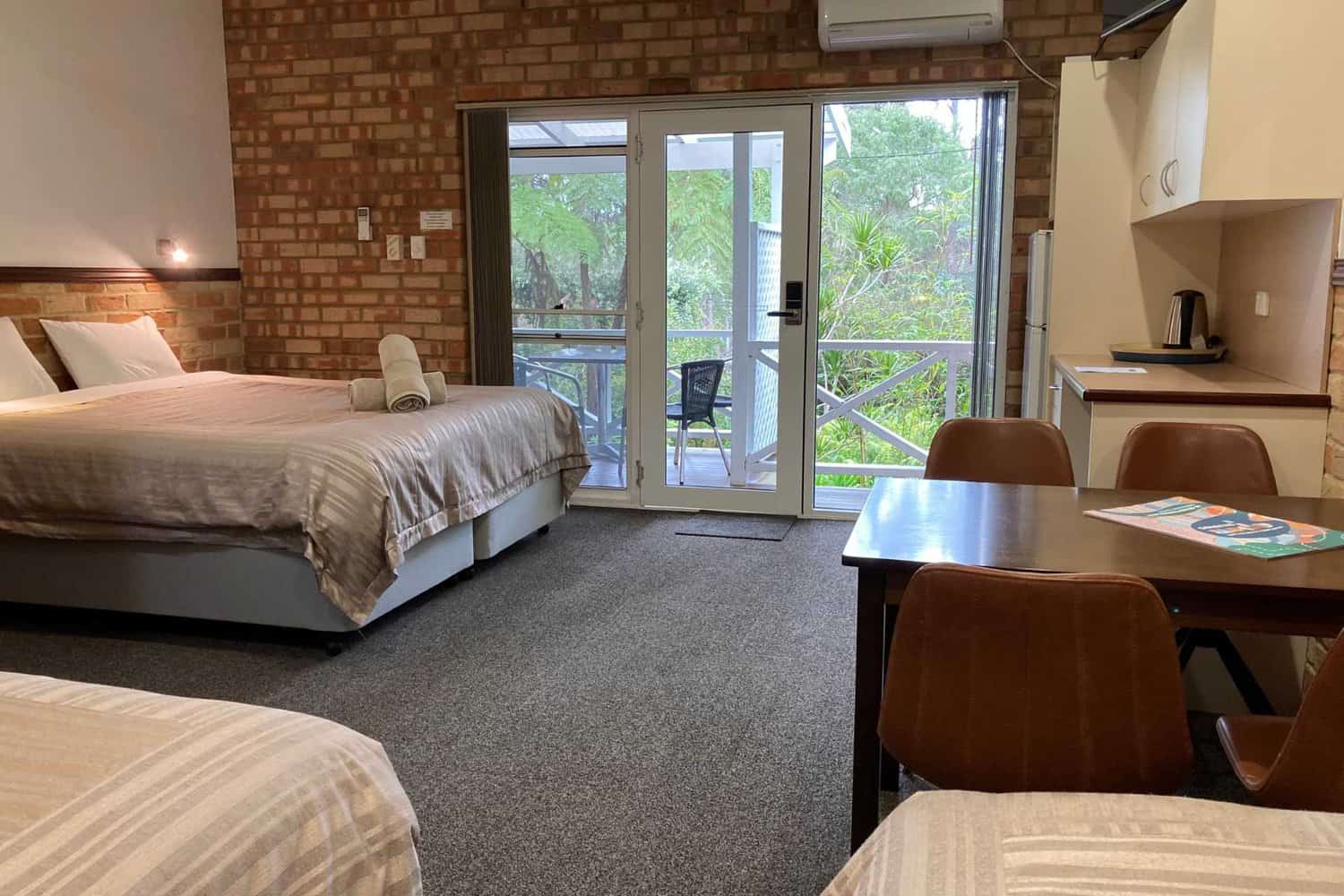 Spacious Big Room at Edge of the Forest Motel featuring a comfortable table and chairs, a well-equipped small kitchenette, and a window offering serene forest views.