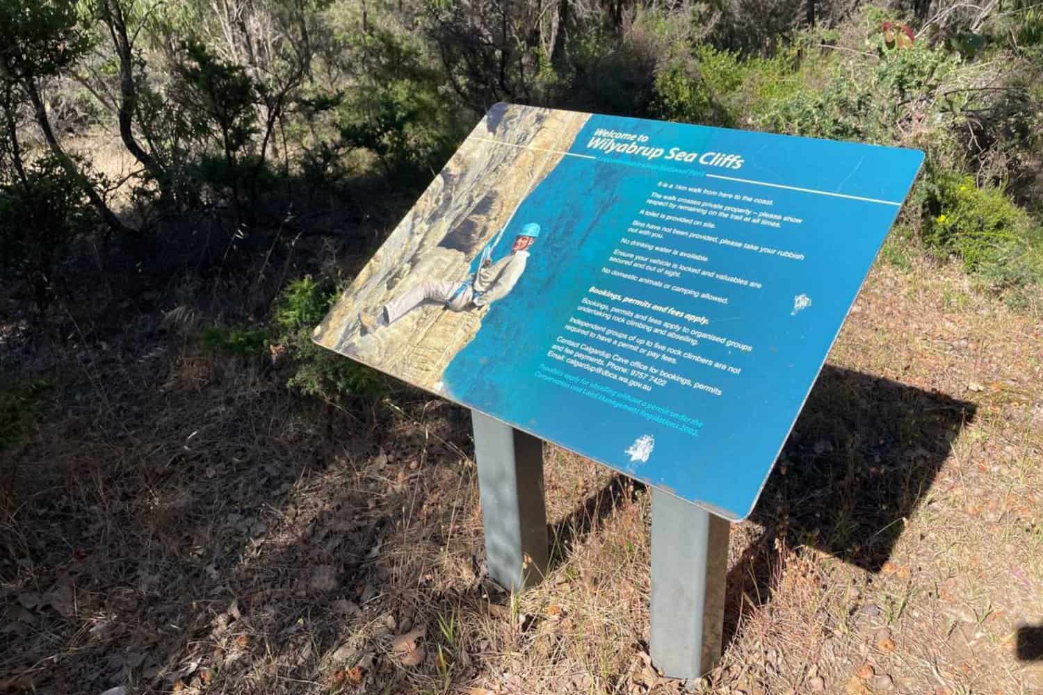 Informational signboard titled 'Welcome to Wilyabrup Sea Cliffs' with a map and details about the cliffs, set against a backdrop of local vegetation, in the natural bushland environment.