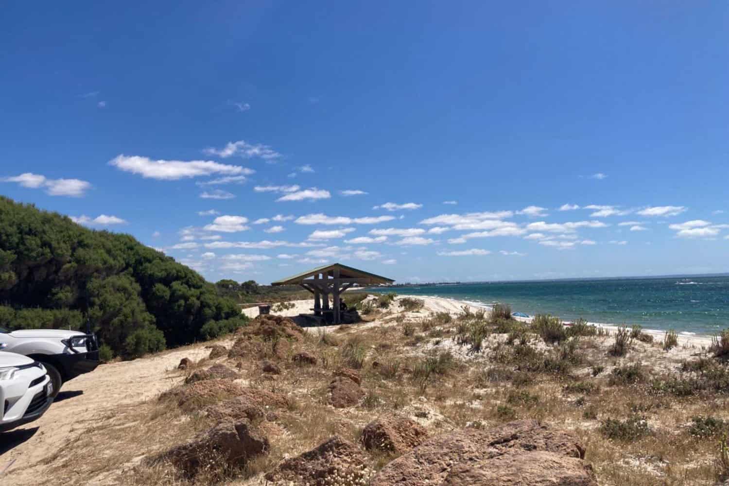 Picnic area overlooking the dunes and clear waters of Busselton beaches with a bright blue sky above.