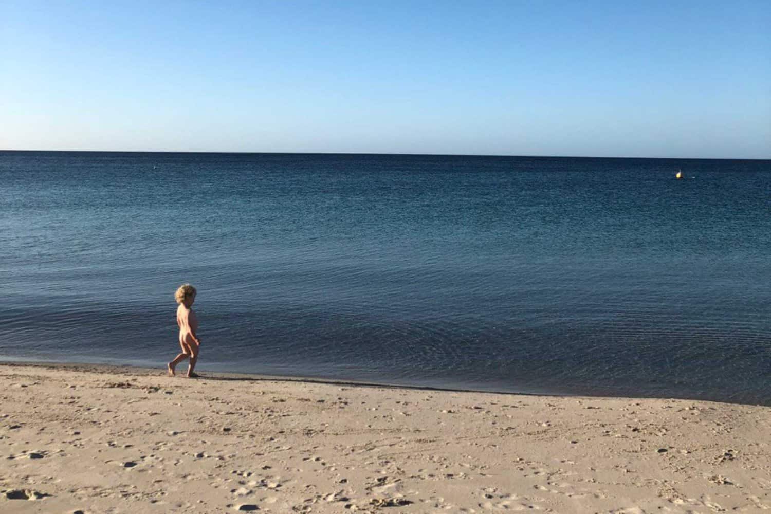 Child standing on the shore of Busselton beaches, looking out at the calm sea on a clear day.