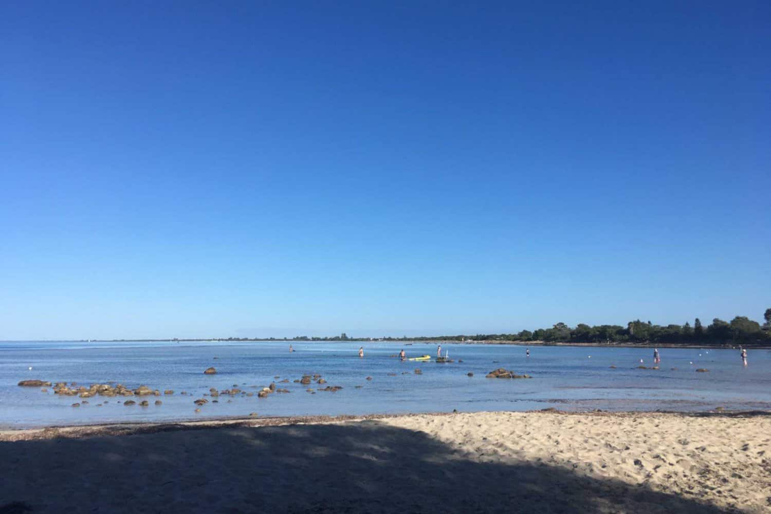 Calm waters and scattered rocks along the Dunsborough Foreshore, under the clear blue sky.