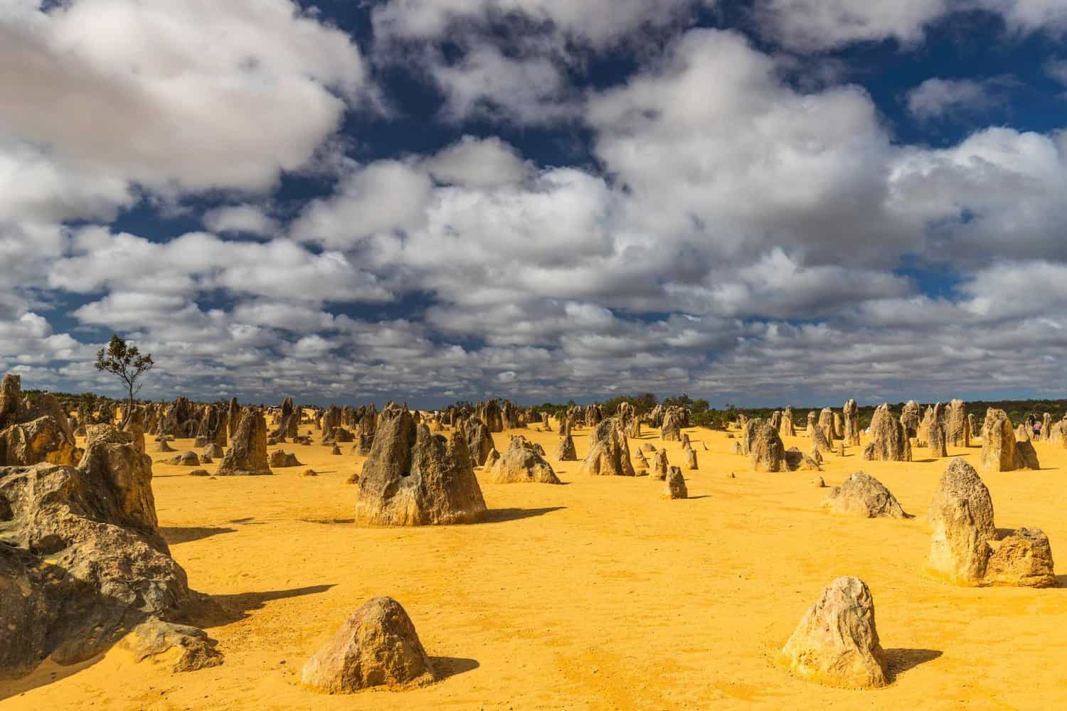 Breathtaking view of the Pinnacles Desert on the Perth to Exmouth journey, featuring unique limestone formations under a dramatic cloudy sky, showcasing the region's natural wonders