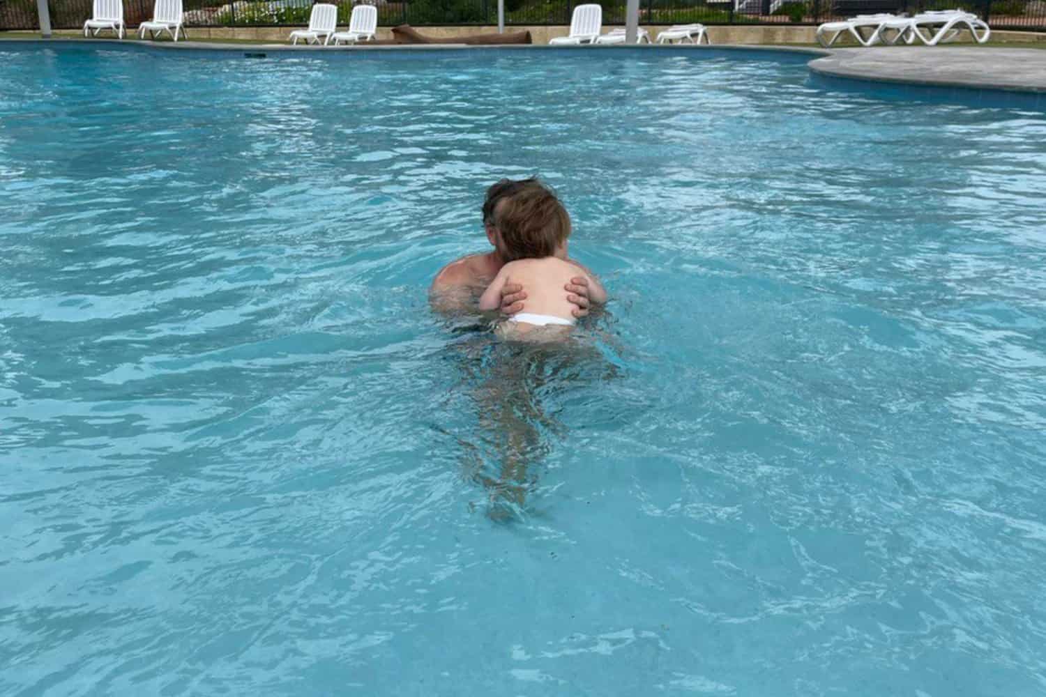 A person enjoying a relaxing swim in a tranquil pool at the RAC Resort in Cervantes, captured from behind, with the individual's back partially submerged in the clear blue water.