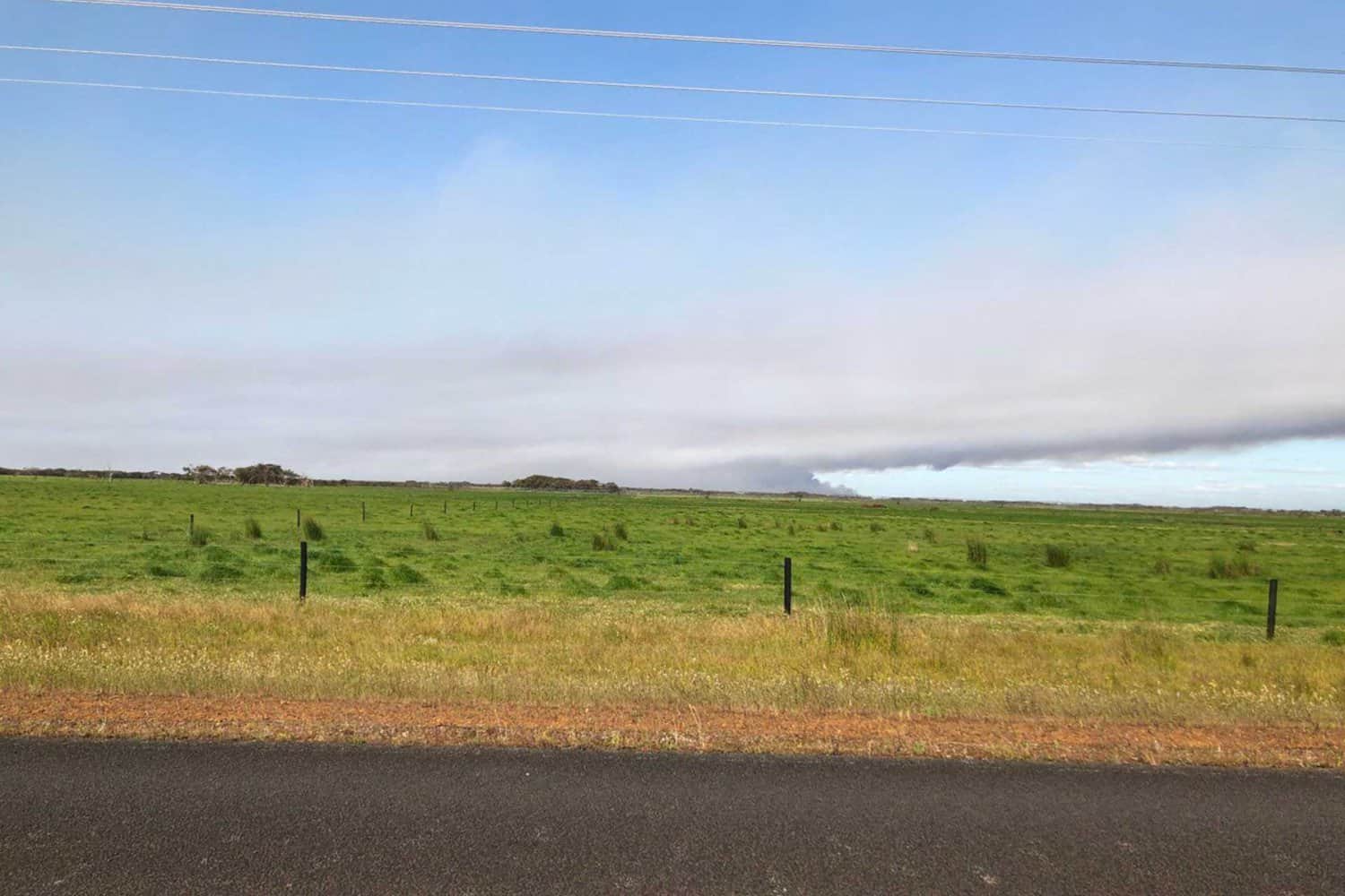 Vast, open grassland stretches to the horizon under a cloud-streaked sky, seen from a roadside perspective in rural Australia, conveying the expansive and tranquil landscape typical of Australia.