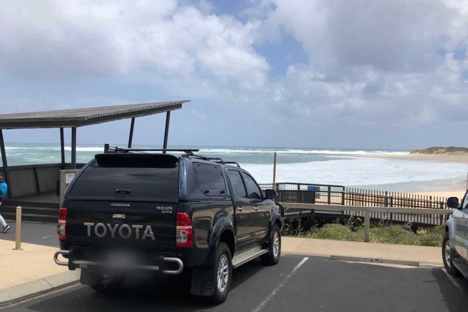 A Toyota Hilux parked near a coastal viewing area at Margaret River, with the rough surf of the ocean in the background, ready for a day of beach activities or fishing.