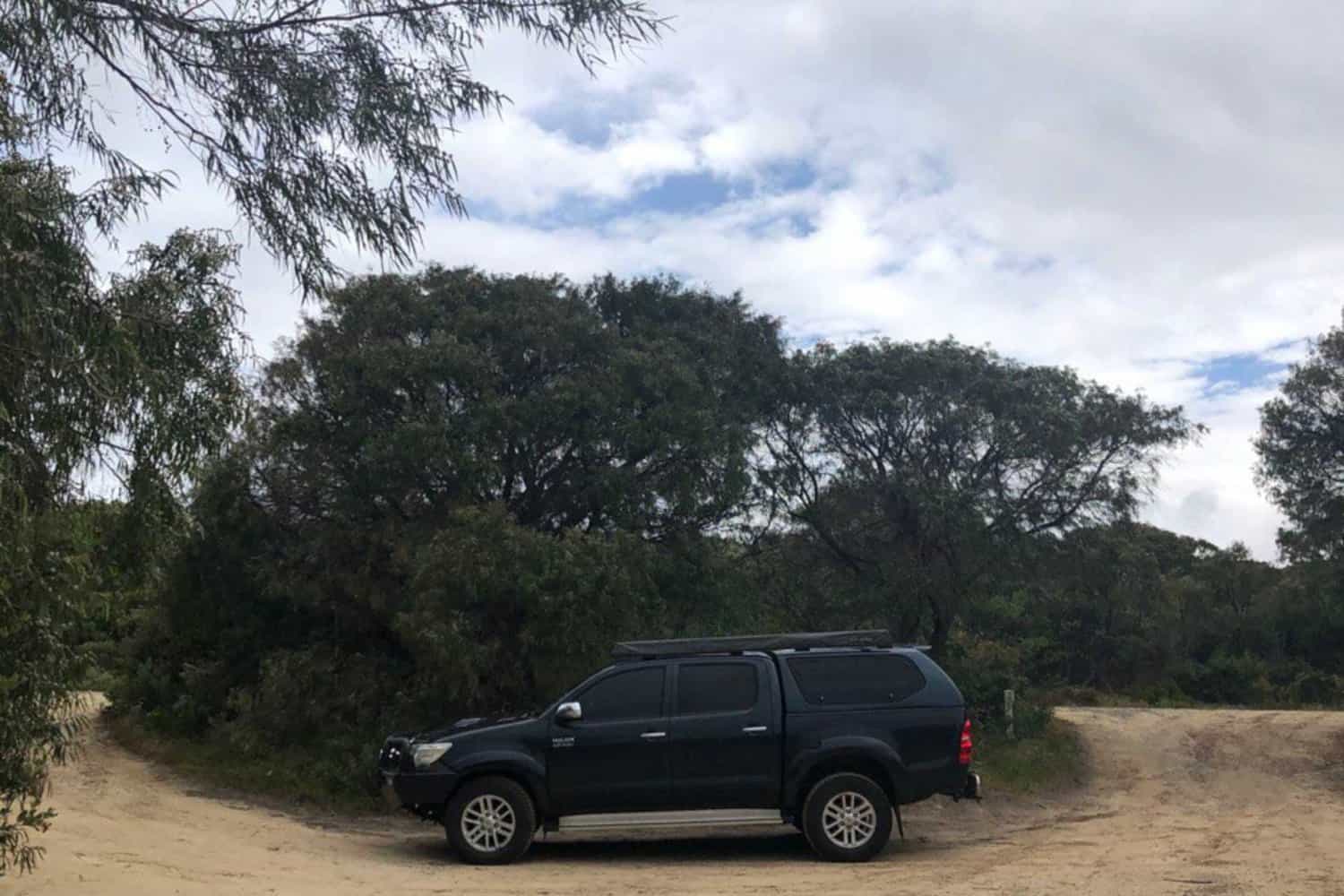 A black SUV parked on a sandy trail surrounded by dense Australian bushland under an overcast sky, indicating a day out in the natural landscapes of Margaret River.