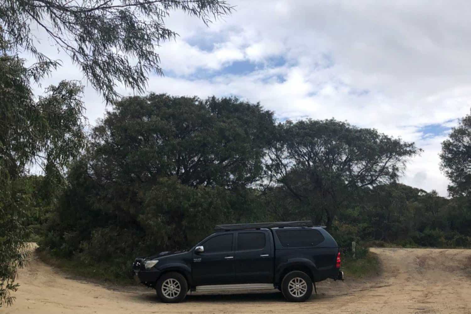 A rugged black Toyota 4x4 hire car parked on a sandy path surrounded by native bushland, evoking the spirit of adventure in Margaret River's natural landscape.