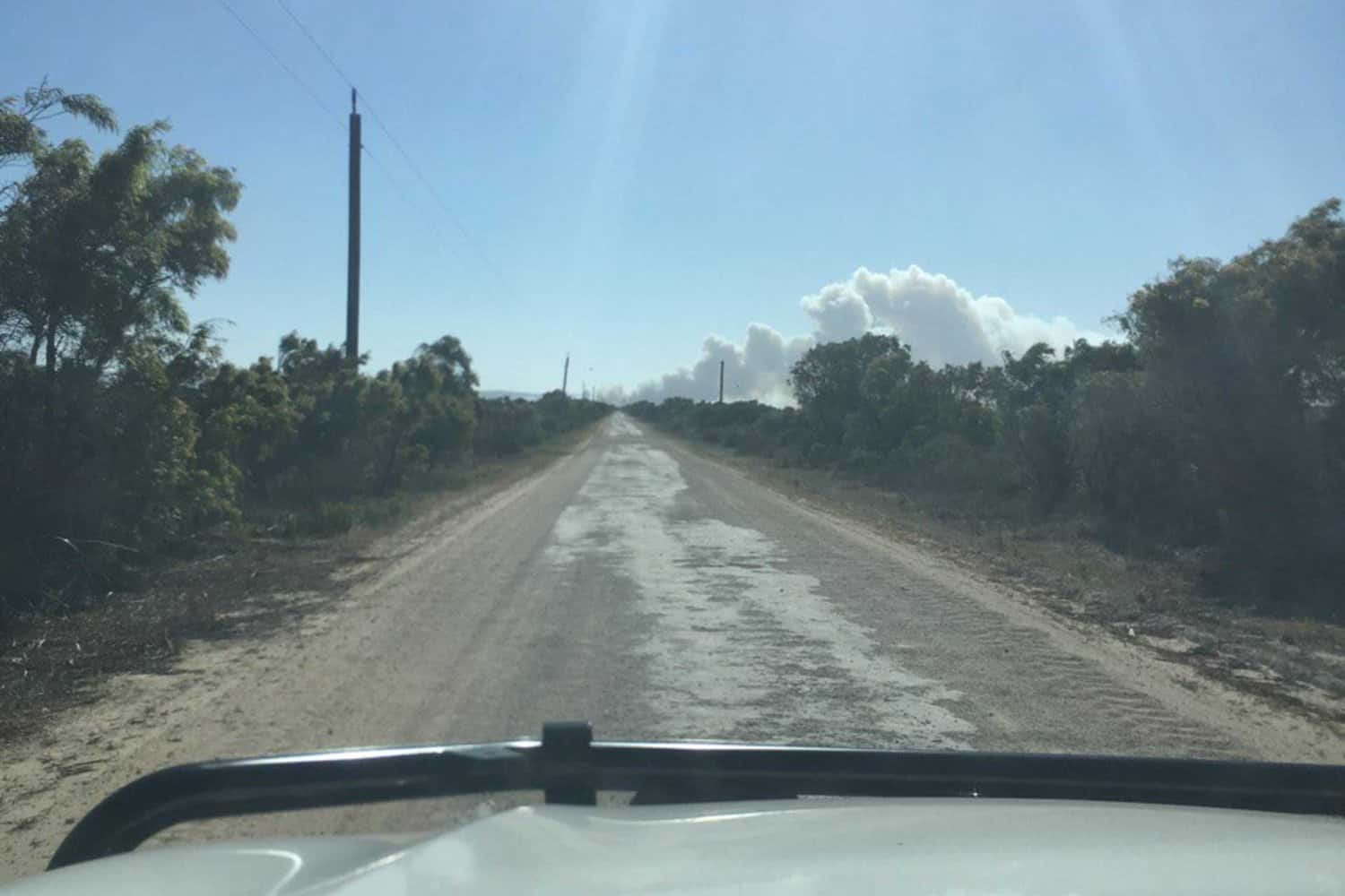 Driver's perspective of a long dirt road ahead, flanked by native shrubbery under the bright Australian sun near Margaret River, evoking a sense of adventure and exploration.