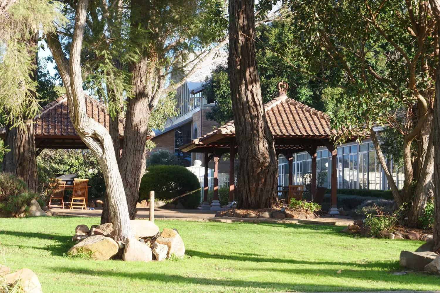 Beautiful full form of hotel courtyard featuring lush green grass, tall trees, and charming gazebos, creating a serene and relaxing atmosphere for guests.