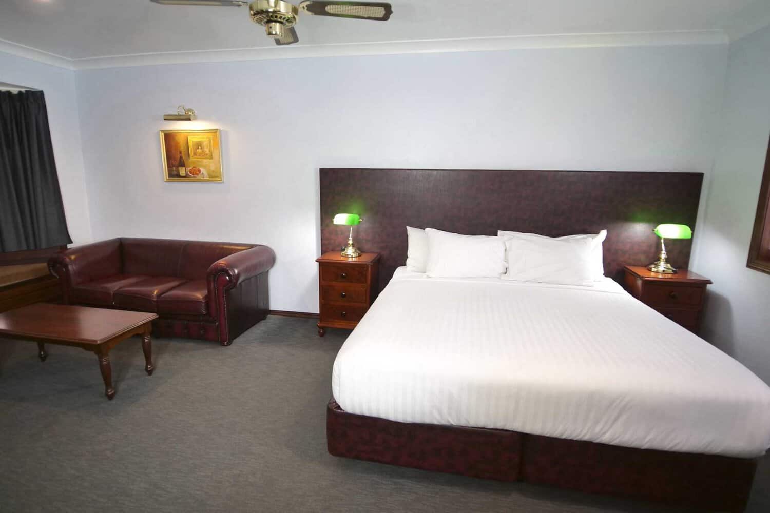 Spacious and well-appointed hotel room featuring a comfortable bed, cozy couch, stylish coffee table, and bedside tables with elegant lamps for a welcoming ambiance.