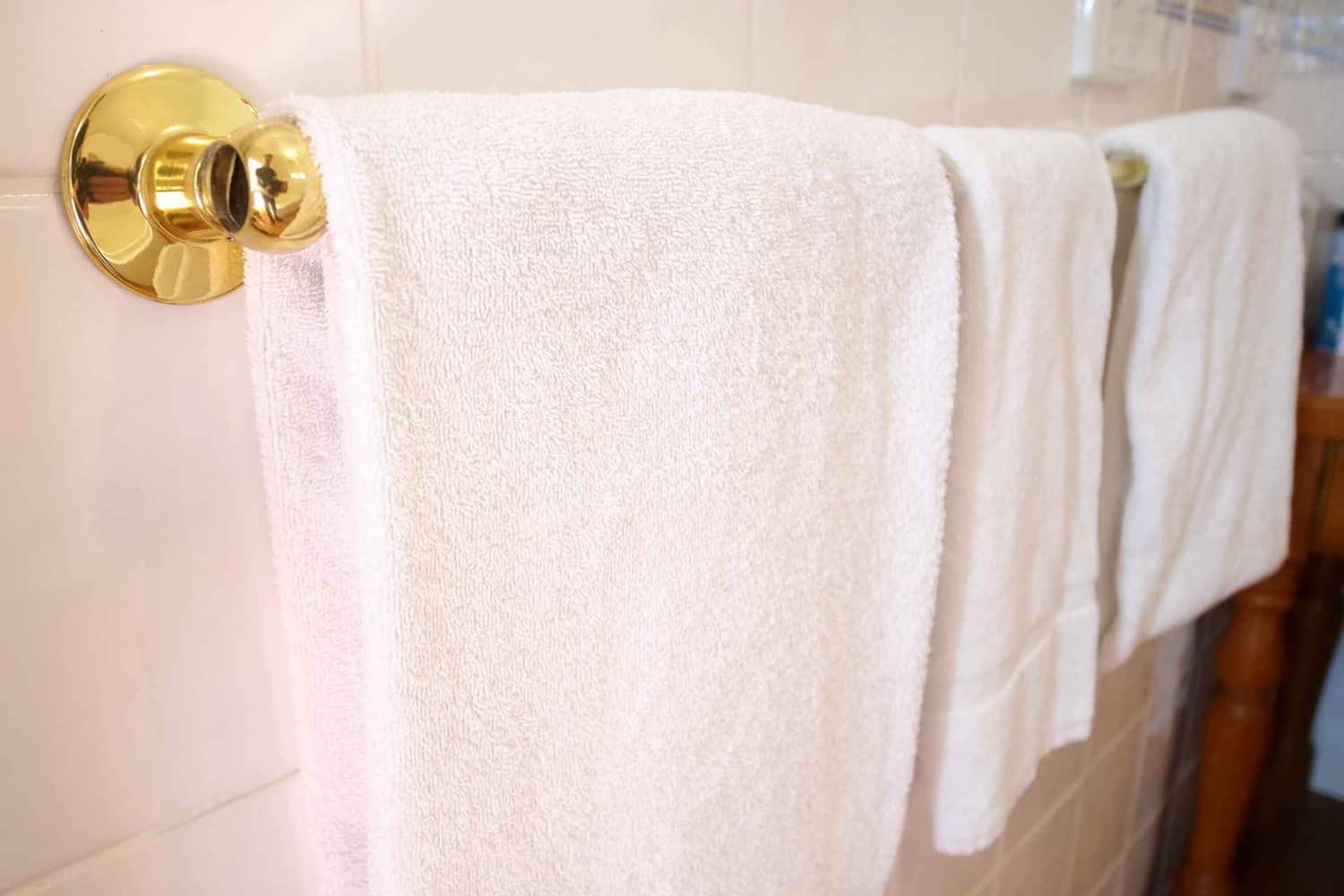 Fresh white towels hanging on a polished gold towel rack in a bathroom, conveying an air of cleanliness and attention to detail in guest accommodations.