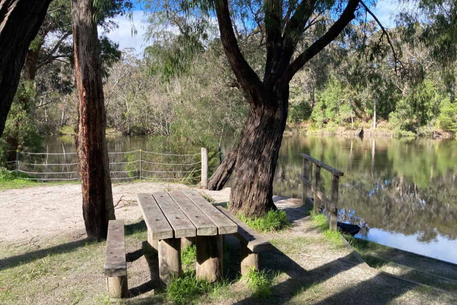 Image from Alexandra Bridge campground, a popular Margaret River caravan park, looking over a picnic table to the river
