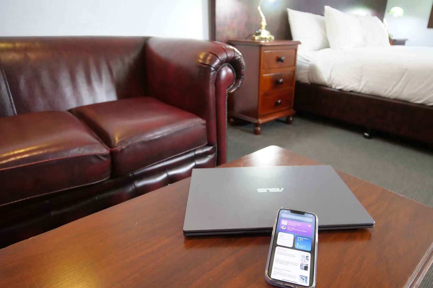 A cozy 2.5-star hotel room featuring a laptop and phone on a coffee table, with a comfortable bed and inviting couch in the background, providing essential amenities for a budget-friendly stay.