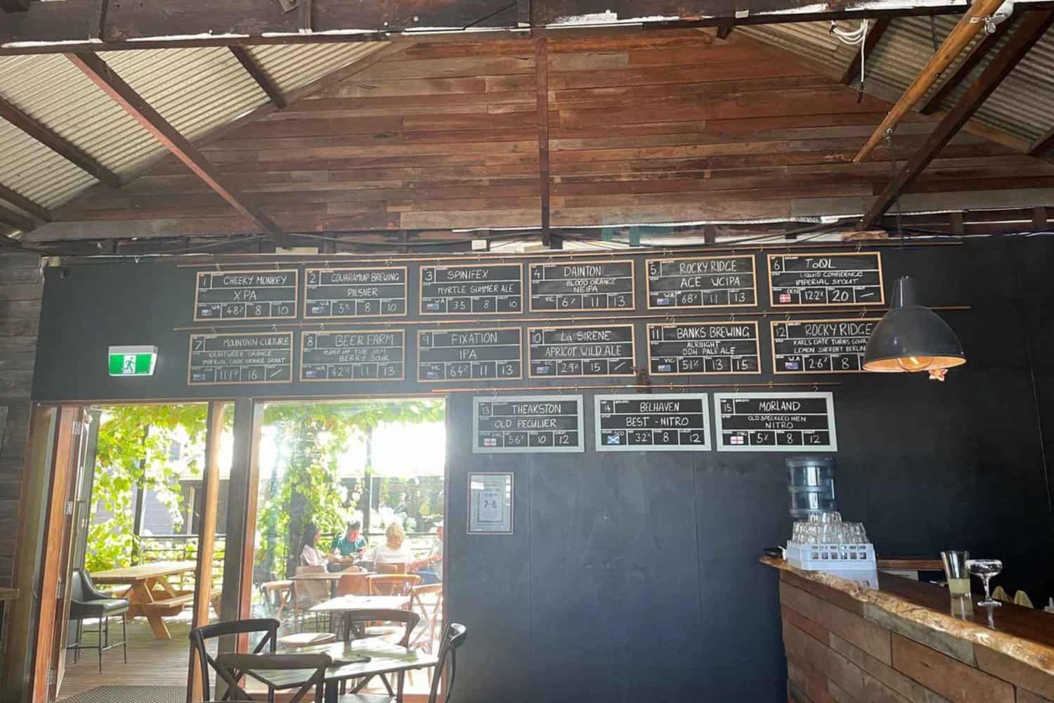 A price wall at the Tap House in Cowaramup showcasing all the different types of local beers on tap. The wall features a list of each beer's name, alcohol percentage, and price per pint. The labels and fonts are artistic and eye-catching, making it easy for customers to choose their favorite brew.