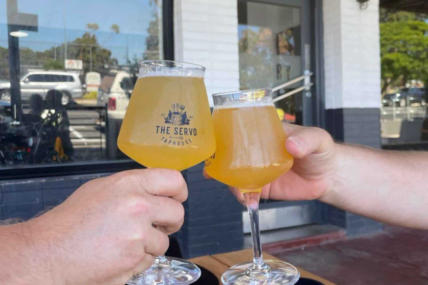 A husband and wife sitting at a local Margaret River bar, clinking their beers together. The couple is enjoying each other's company and the social atmosphere of the bar. 