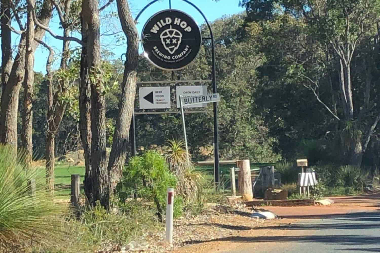 A view of the Wild Hop Brewing Company sign as taken from the road, showcasing the brewery's logo and name prominently displayed on a black metal sign with lettering and their logo in the centre.