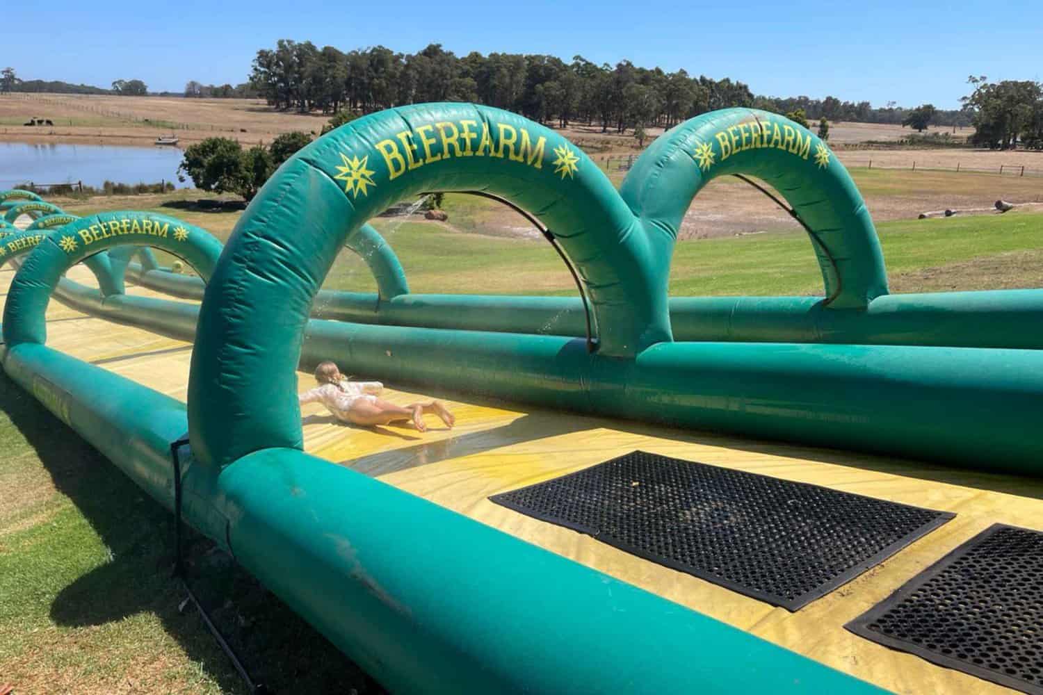 Kids having fun as they slide down a wet and slippery slide at the Beerfarm Margaret River, (one of the best breweries Margaret River!) with water splashing around them and bright smiles on their faces.