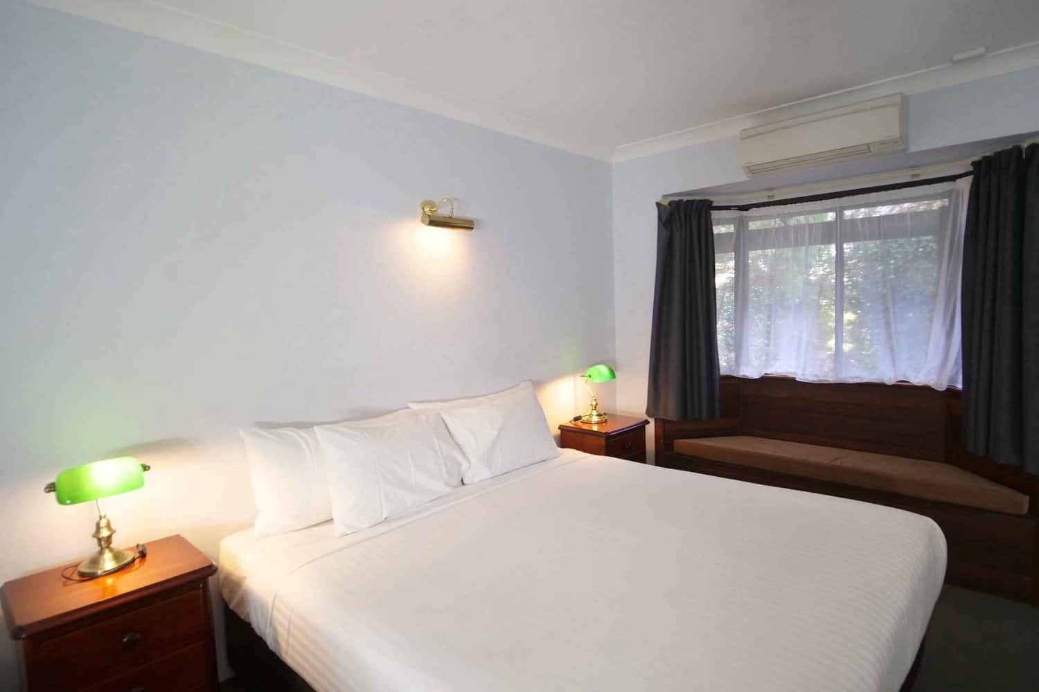 Inviting king size bed in a hotel room, complete with bedside lamps and a window offering natural light, as guests ponder the duration of their stay in such a comfortable and welcoming environment
