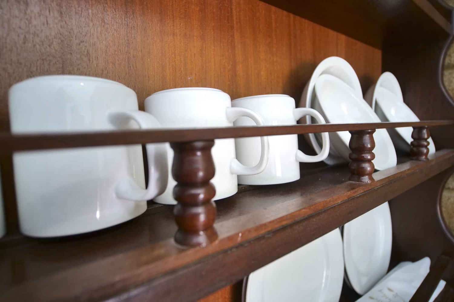 Neatly arranged mugs, plates, bowls, and cutlery on display in a hotel room, showcasing the amenities provided for guests considering extended stays at the hotel
