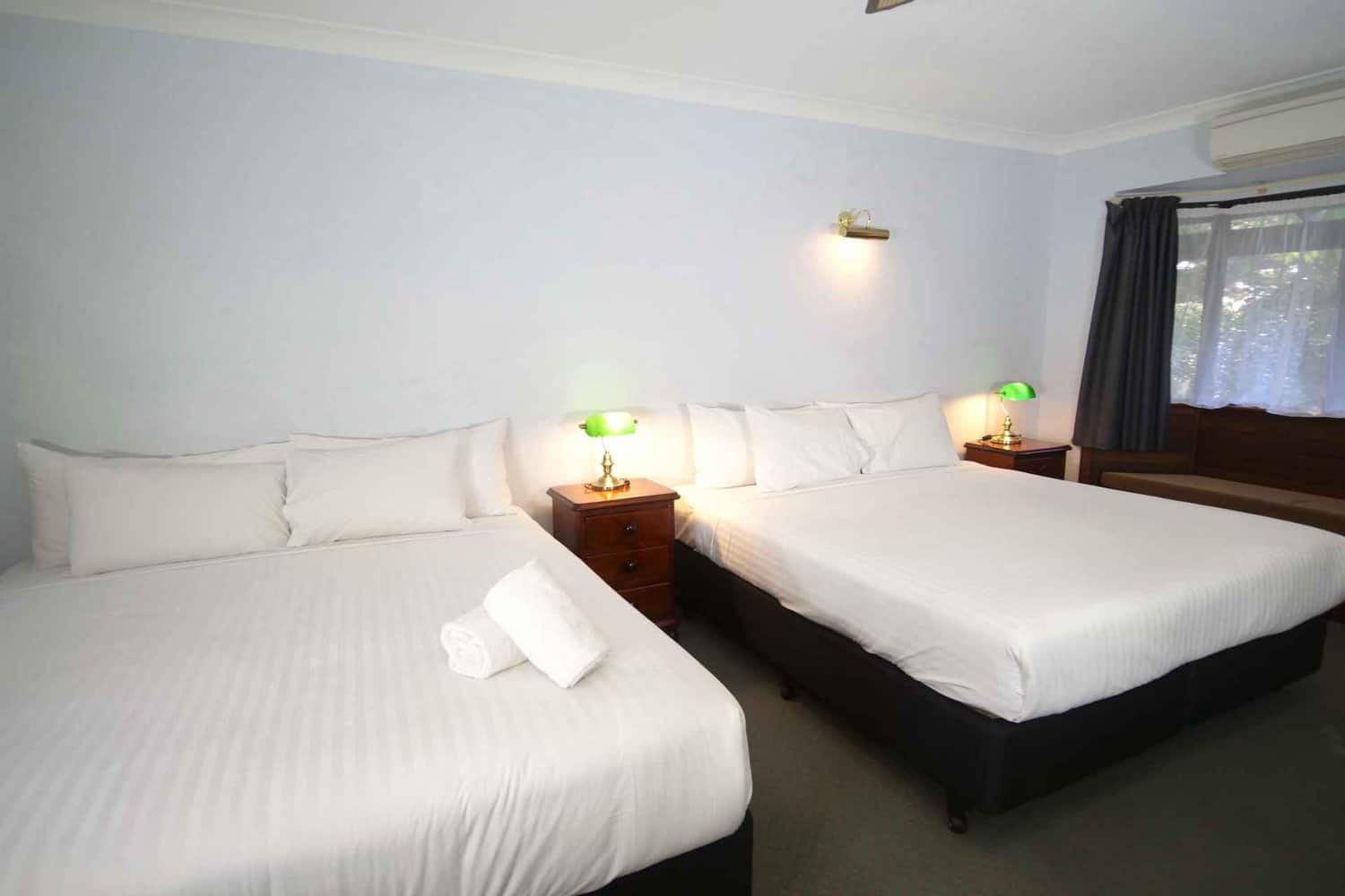 Spacious hotel room featuring two king size beds, side tables with lamps for added comfort, and a window with open curtains allowing natural light to fill the space, inviting guests to consider an extended stay