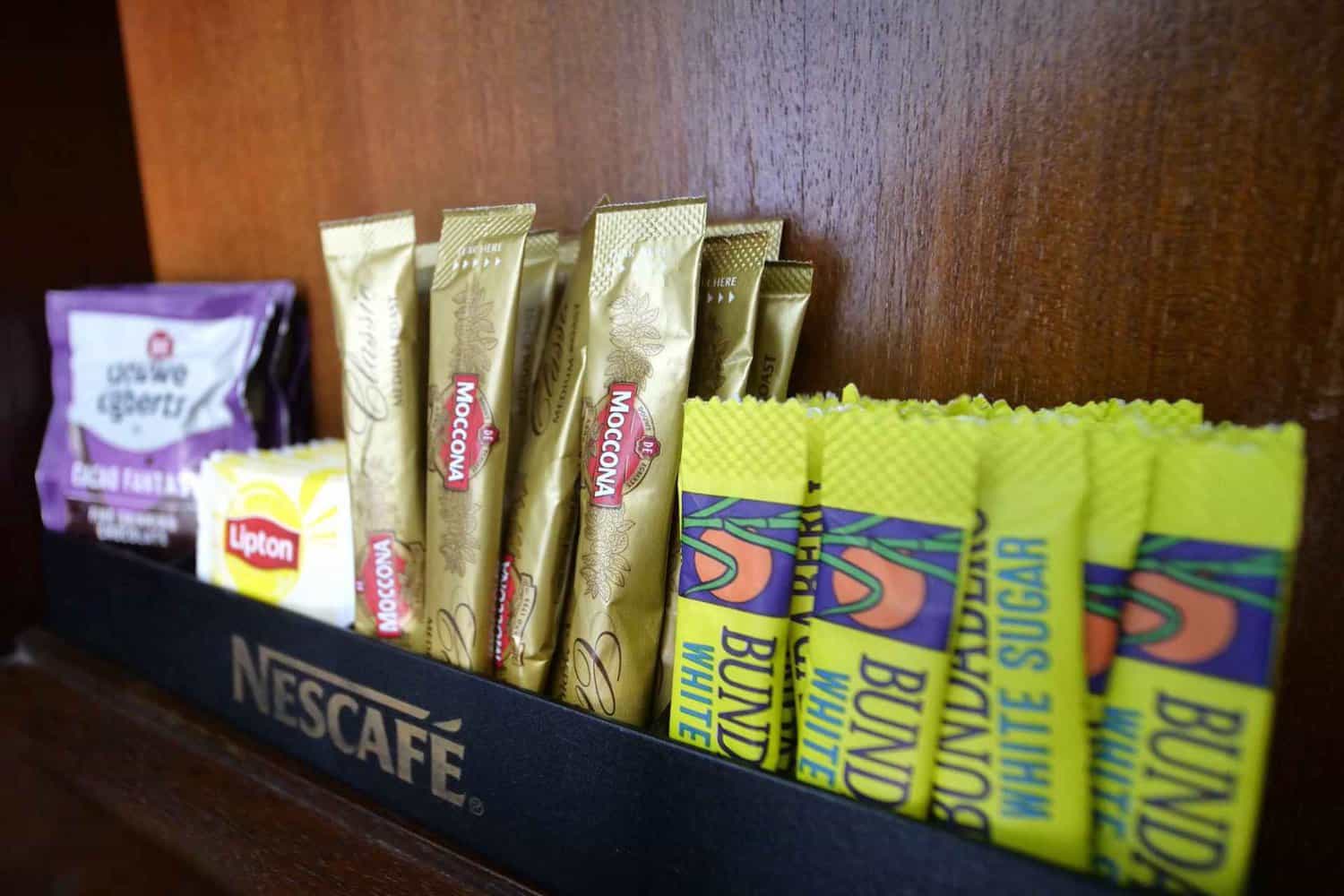 Assortment of sugar sticks, coffee sticks, hot chocolate powder, and tea bags thoughtfully displayed in a hotel room, offering a variety of beverage options for guests during their extended stay