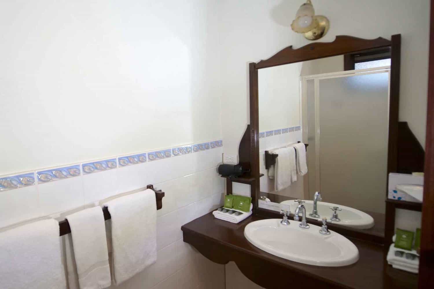 Well-appointed hotel bathroom featuring fresh towels on a rail, an array of bathroom amenities for guests' convenience, and a large mirror over the sink, reflecting the comfort and hospitality provided during an extended stay