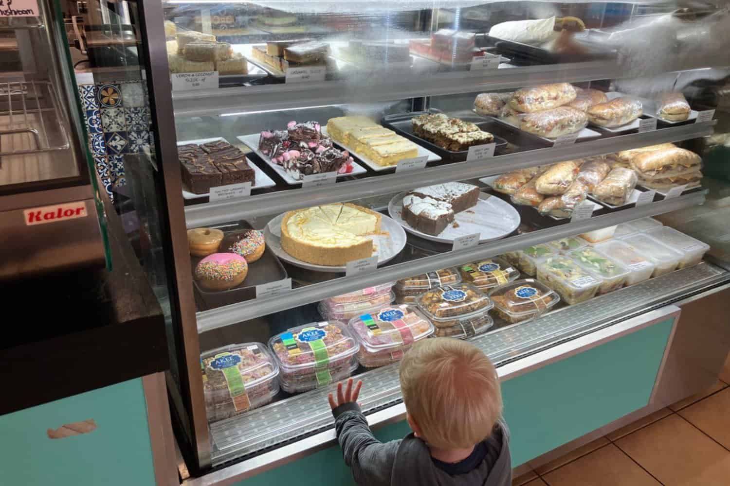 A small child excitedly admires the delicious rolls, salads, and cakes at a Margaret River cafe, known for serving the best coffee in the region.