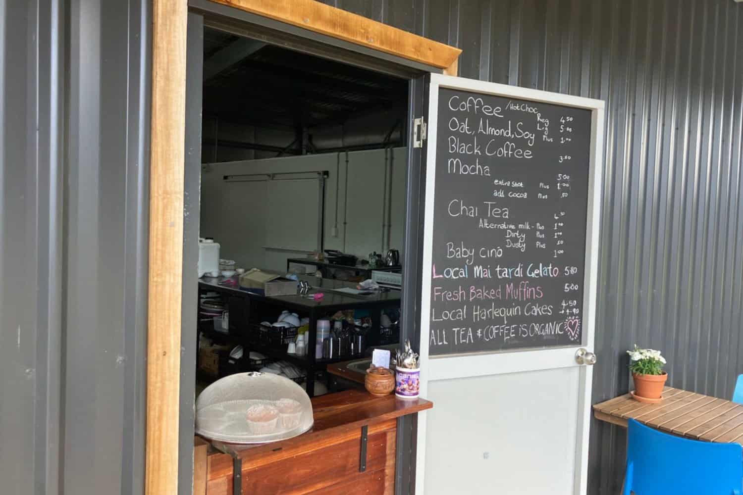 A charming outdoor coffee counter in Margaret River, known for serving the best coffee in town. The image captures a walk-up window with a hole in the wall where customers can place their orders. A chalkboard menu displays the available options, while freshly baked muffins are showcased on the counter for an enticing treat.