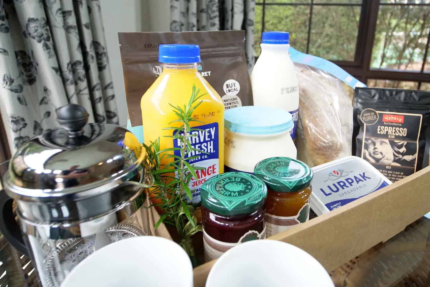 A delicious in-room breakfast spread featuring local Margaret River goods such as orange juice, coffee, yogurt, jams, butter, and more, showcasing the difference between hotel and restaurant experiences by offering personalized dining in a comfortable hotel room setting.