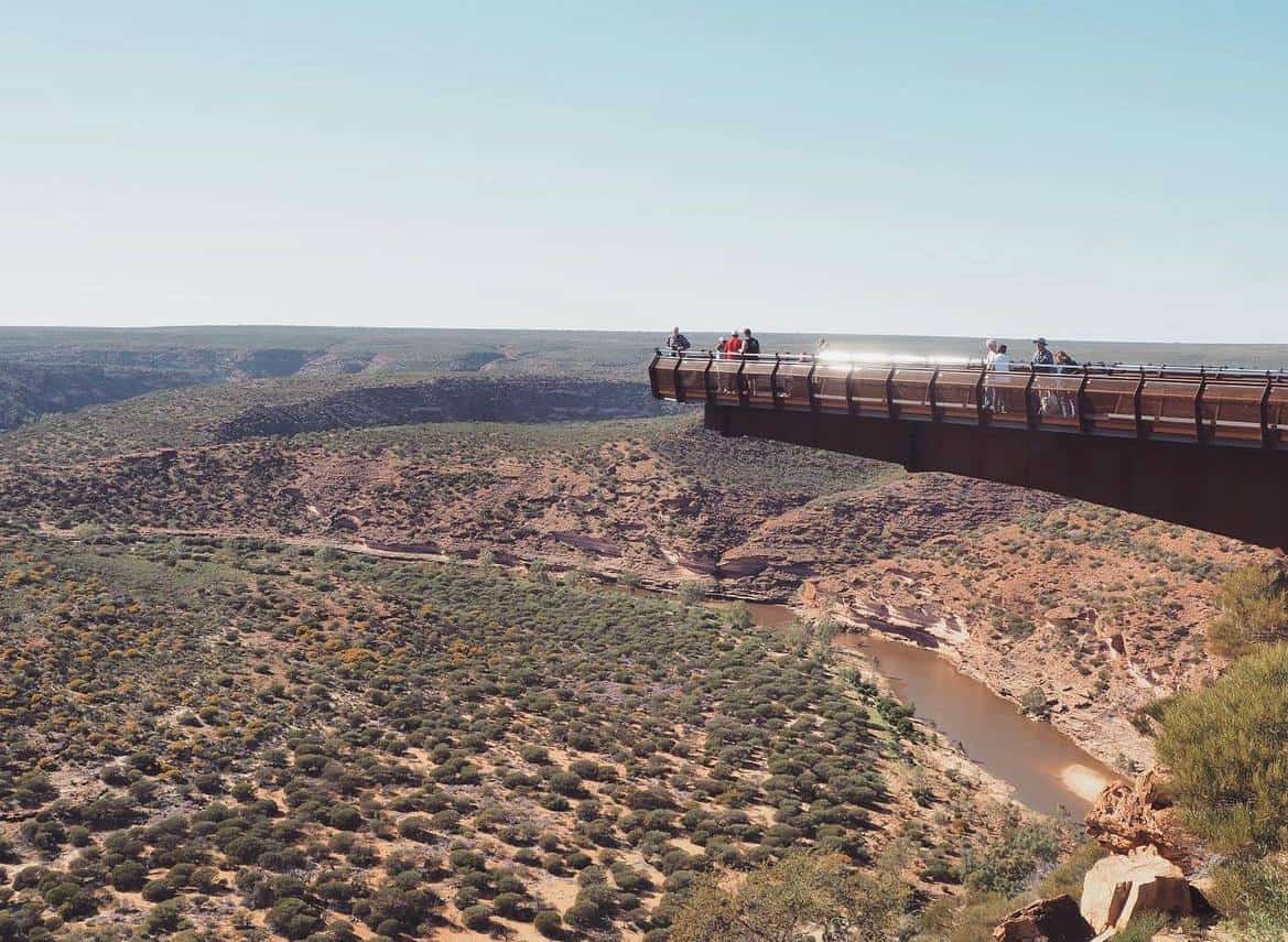 Tourists enjoying the view from a cantilevered lookout over a gorge with a river at its base, along the scenic route from Perth to Kalbarri, illustrating the popular tourist experiences available in Western Australia.