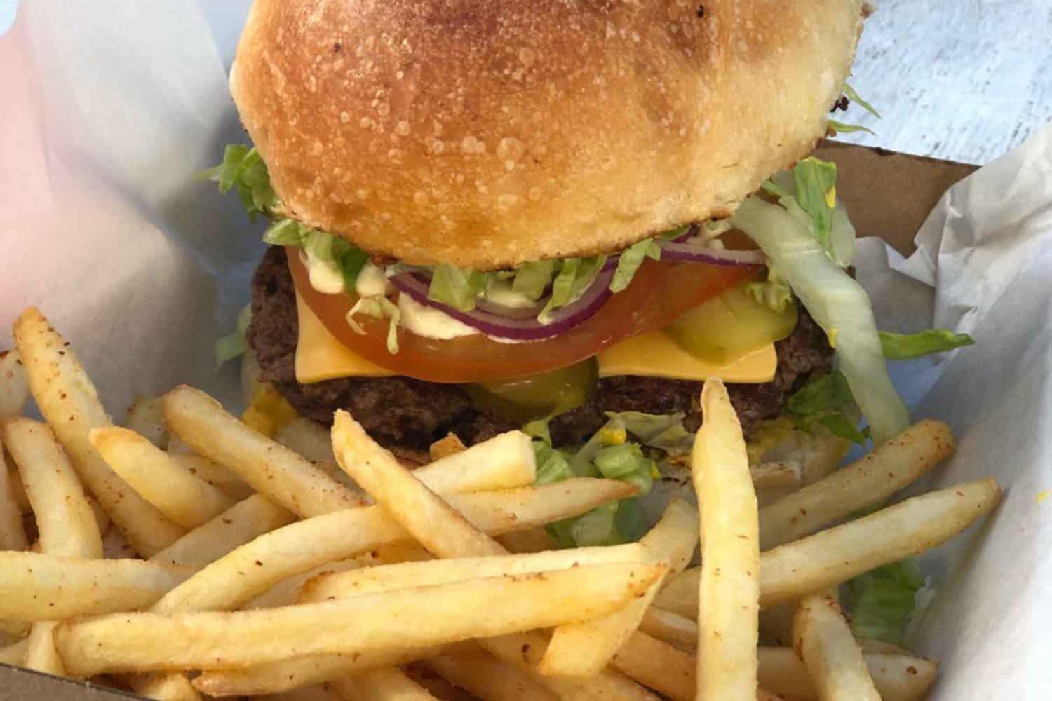 A delicious burger and golden crispy chips neatly placed on a sheet of paper inside a takeaway box, representing a tempting takeaway meal in Margaret River.