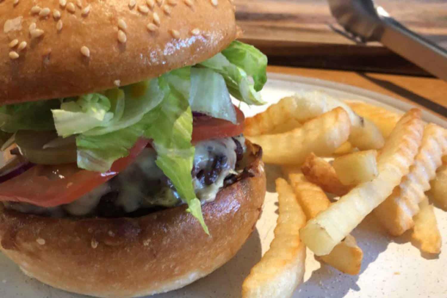 A mouthwatering burger and a side of golden, crispy chips presented in a takeaway setting. The burger is stacked with a juicy patty, fresh lettuce, ripe tomatoes, melted cheese, and savory sauce. The image showcases a delectable takeaway meal option in Margaret River