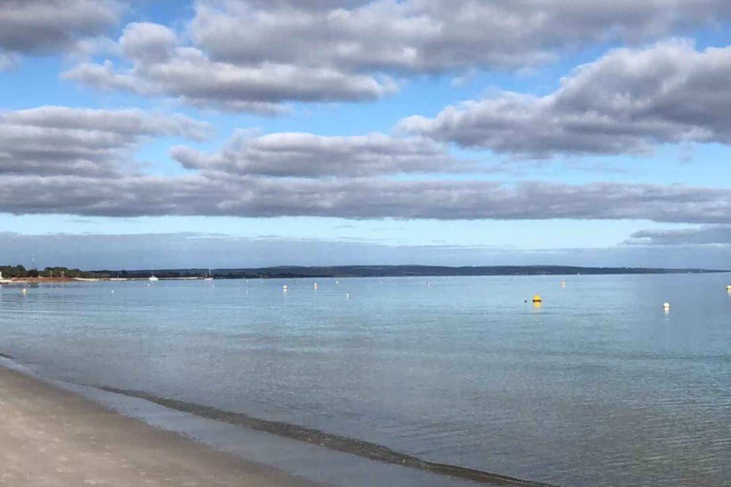 Tranquil waters and cloudy skies at Dunsborough beaches, with distant sailboats and buoys dotting the horizon.