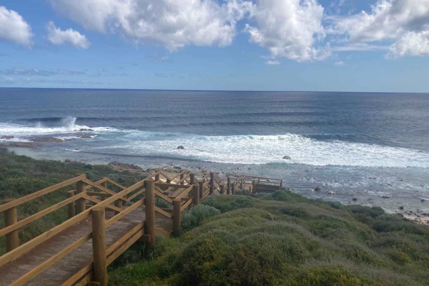 Wooden staircase leading to the rugged coastline of Moses Beach, under a sky with fluffy clouds.