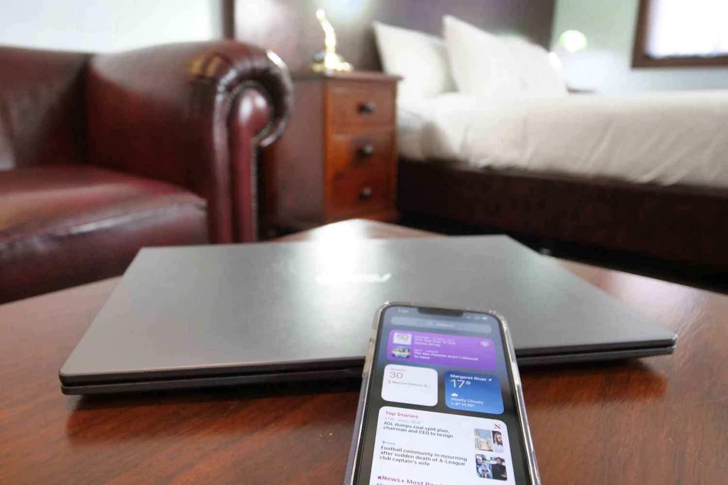 Close-up of a work-friendly setup in a Margaret River accommodation room, featuring a sleek laptop on a wooden table and a smartphone displaying weather in Margaret River, ideal for business travelers deciding on the best time to book.