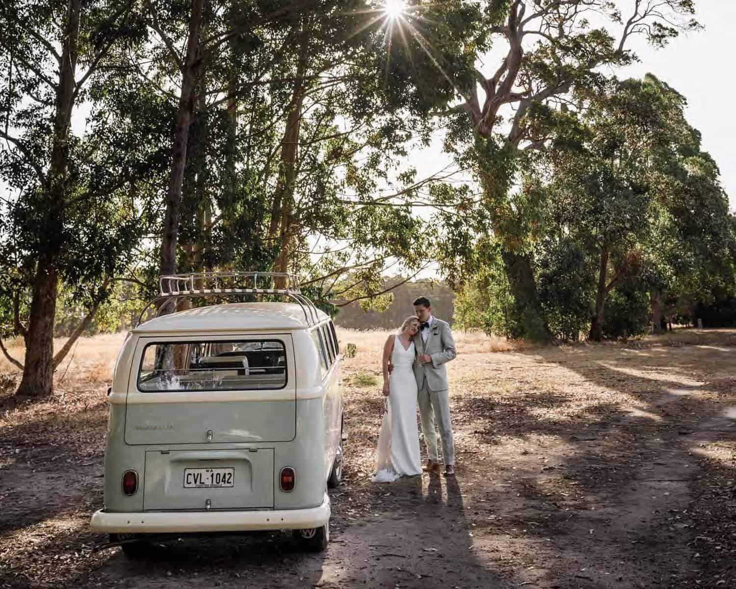 A joyful couple standing together next to a charming vintage van, set against the picturesque backdrop of Margaret River's lush greenery, perfectly capturing the beauty of a Margaret River wedding venue.