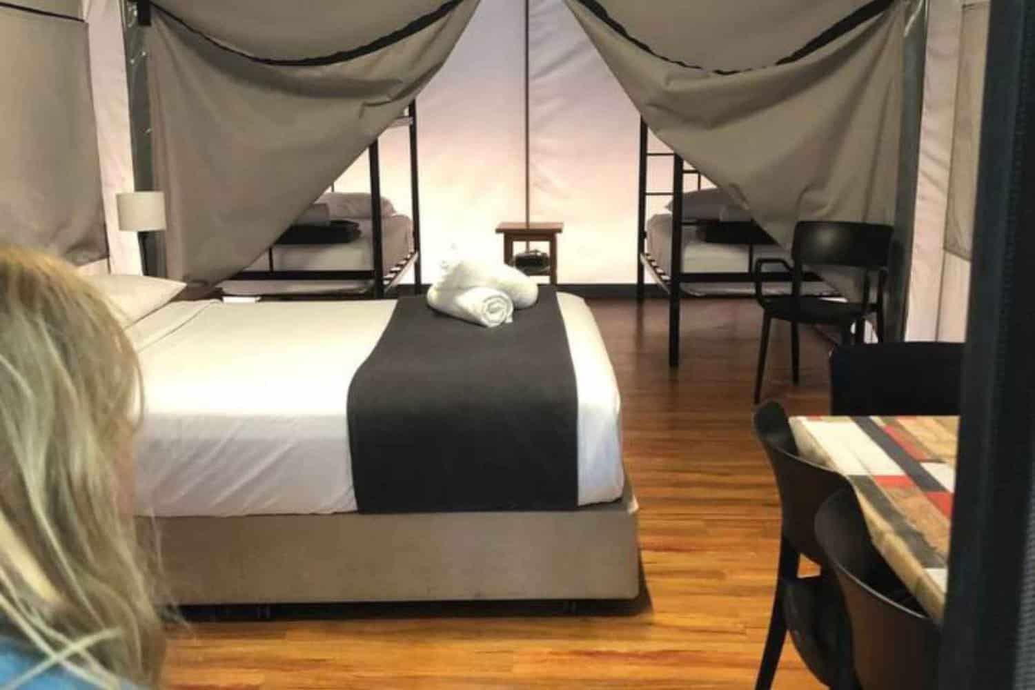 Unique hotel room setup with safari tent-style draping over the beds, wooden flooring, and modern furnishings, creating an adventurous yet luxurious atmosphere for guests.